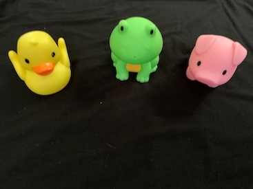 The image depicts uncluttered scene featuring a toy duck, frog and pig set upon a black cloth. 