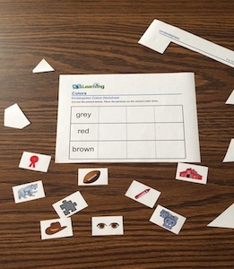 The image features a worksheet placed on a wooden desk with all of the pieces of the picture images strewn around without order. 